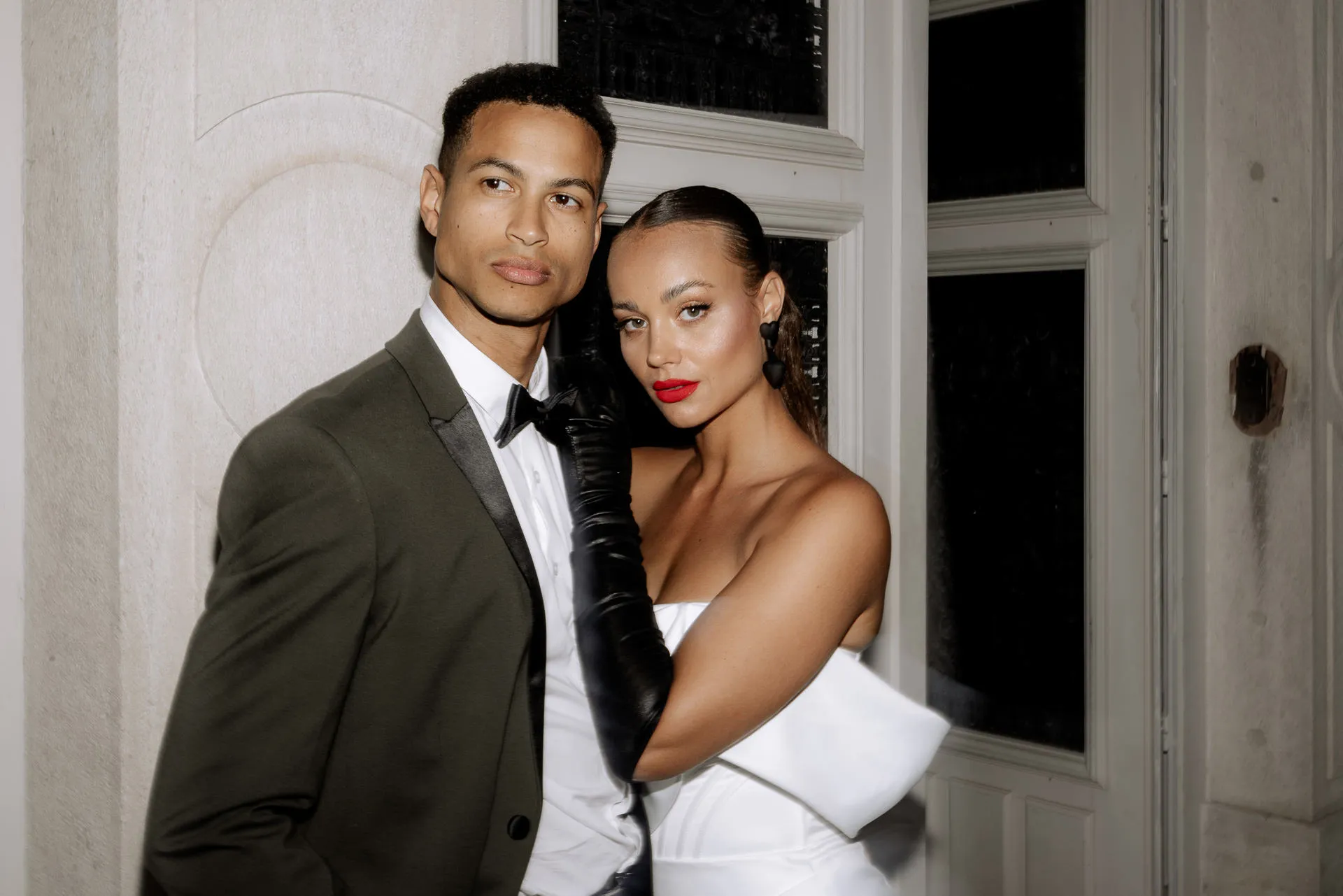 Fashion bridal couple portrait in front of French doors at Chateau de Varennes with olive green suit and black gloves